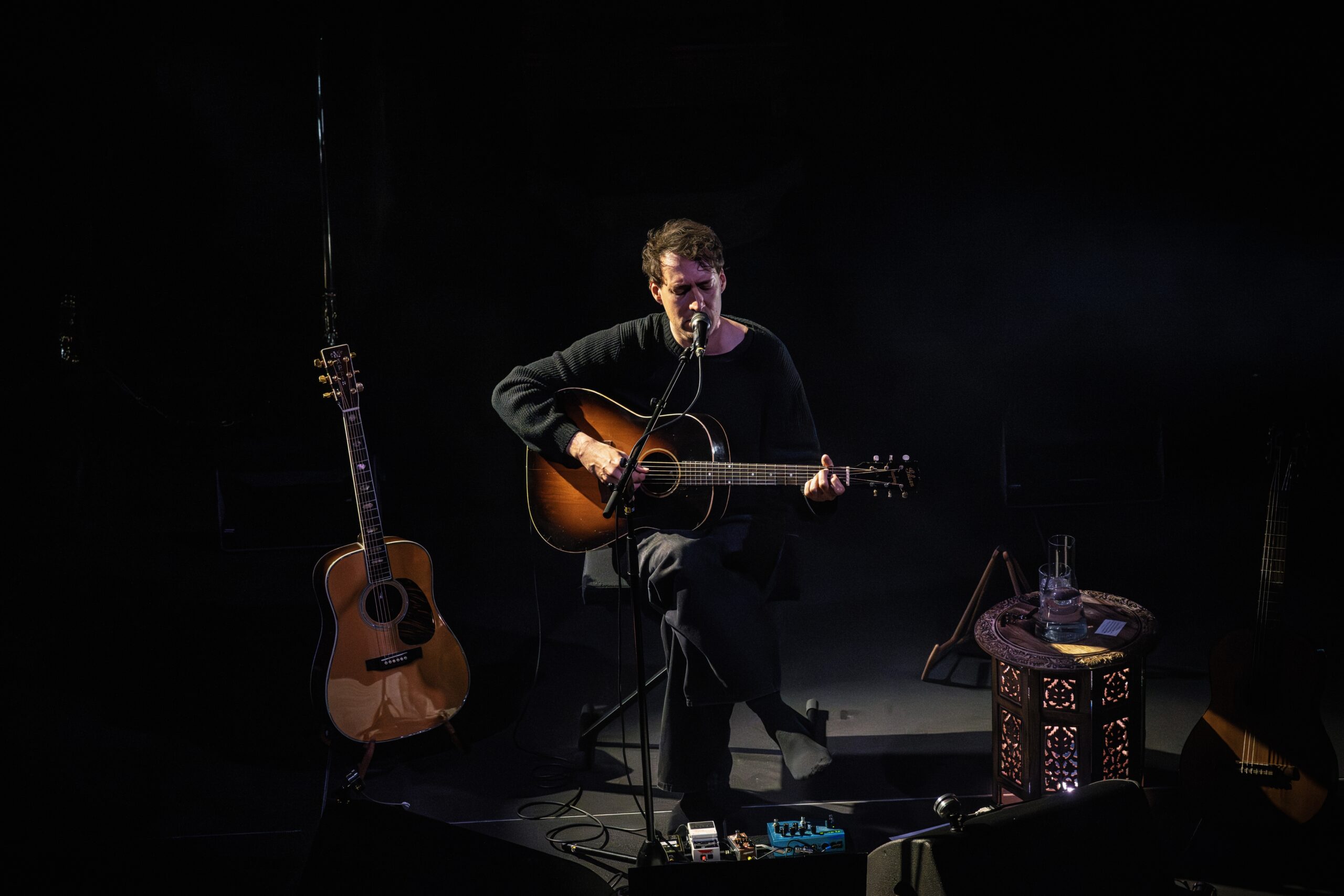 Eloi Youssef staand met akoestische gitaar in warm schijnwerperlicht in Arminius Rotterdam