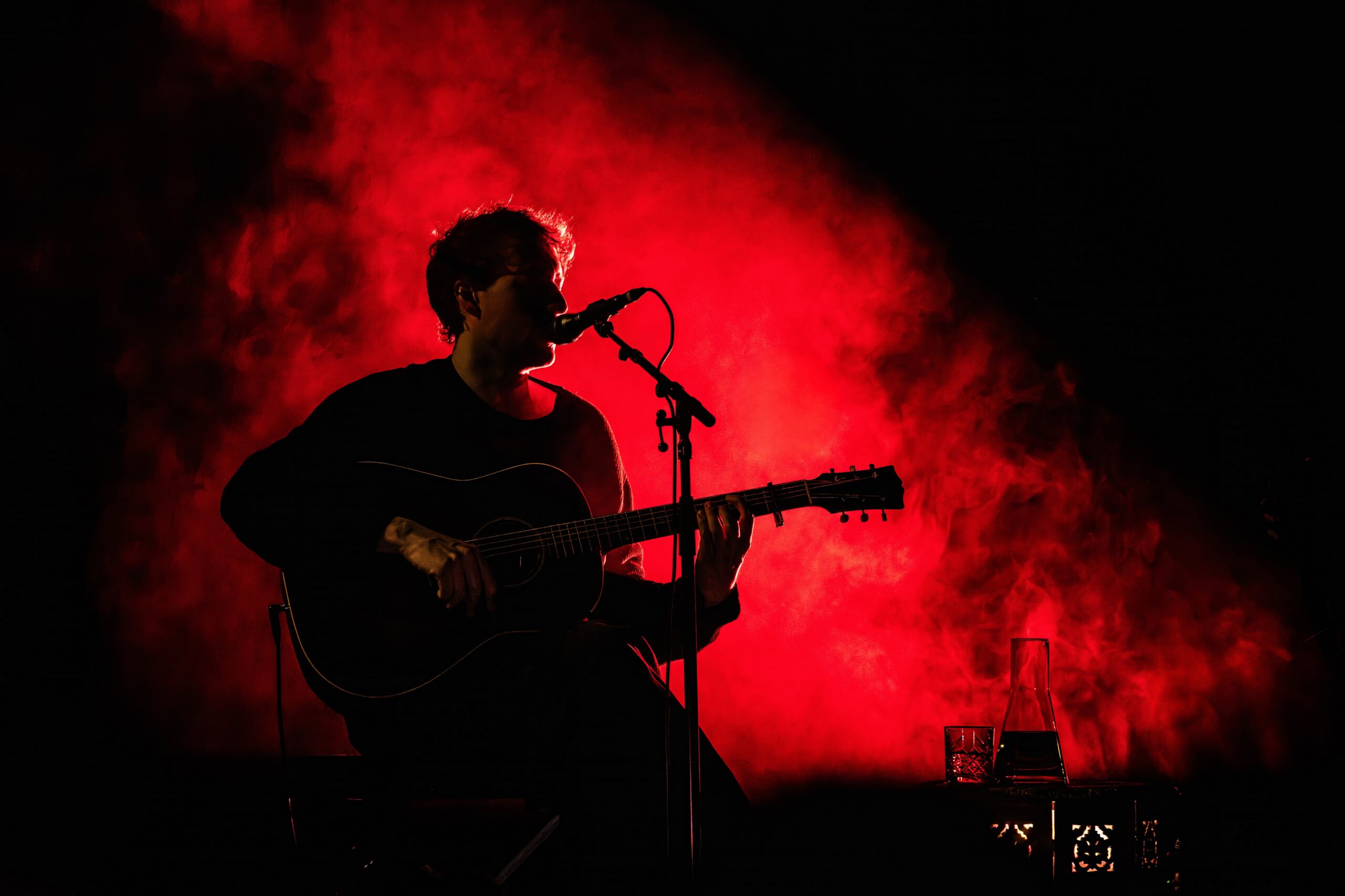Eloi Youssef in rood tegenlicht tijdens zijn akoestische set
