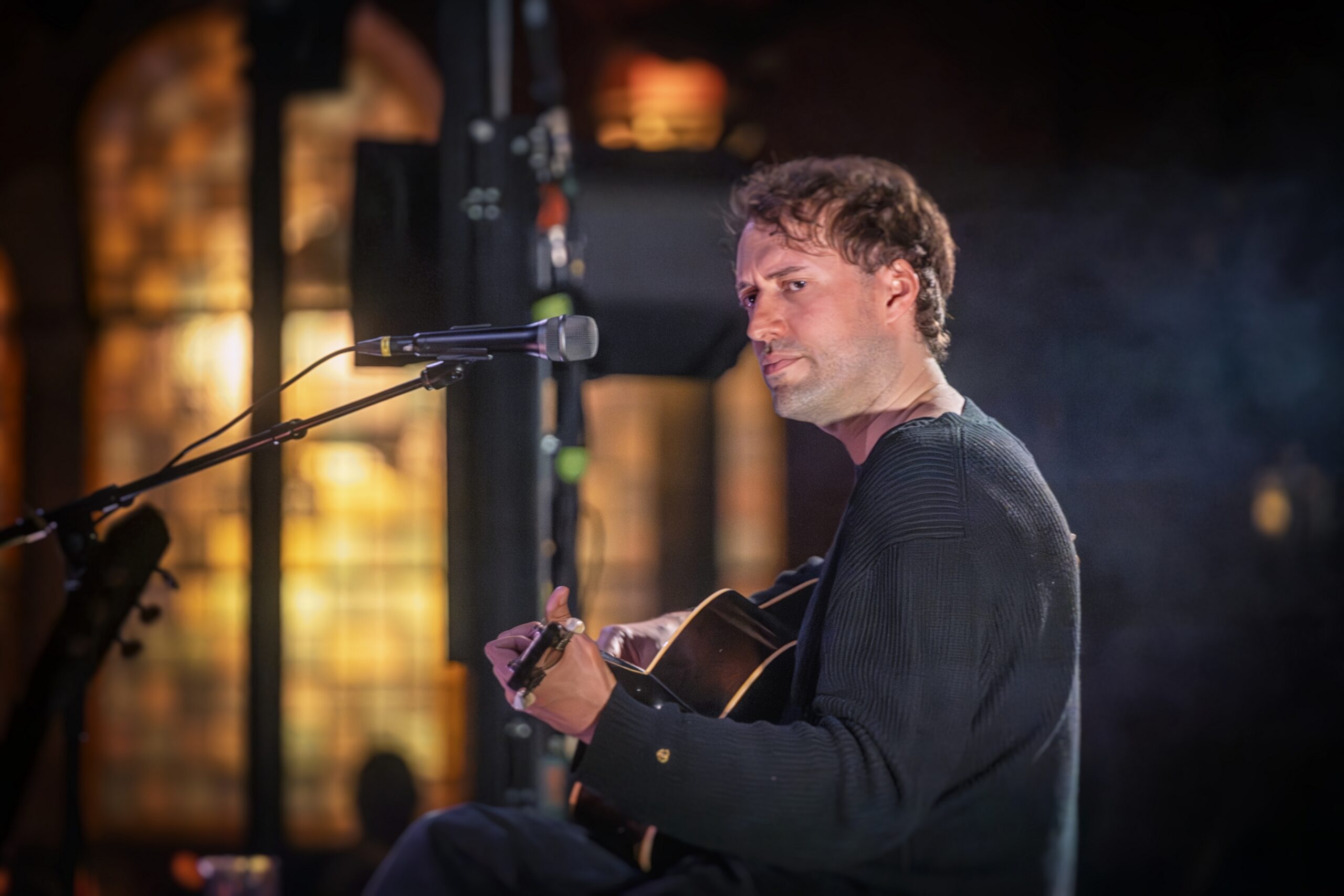 Close-up van Eloi Youssef terwijl hij zingt in warm licht tijdens zijn akoestische set