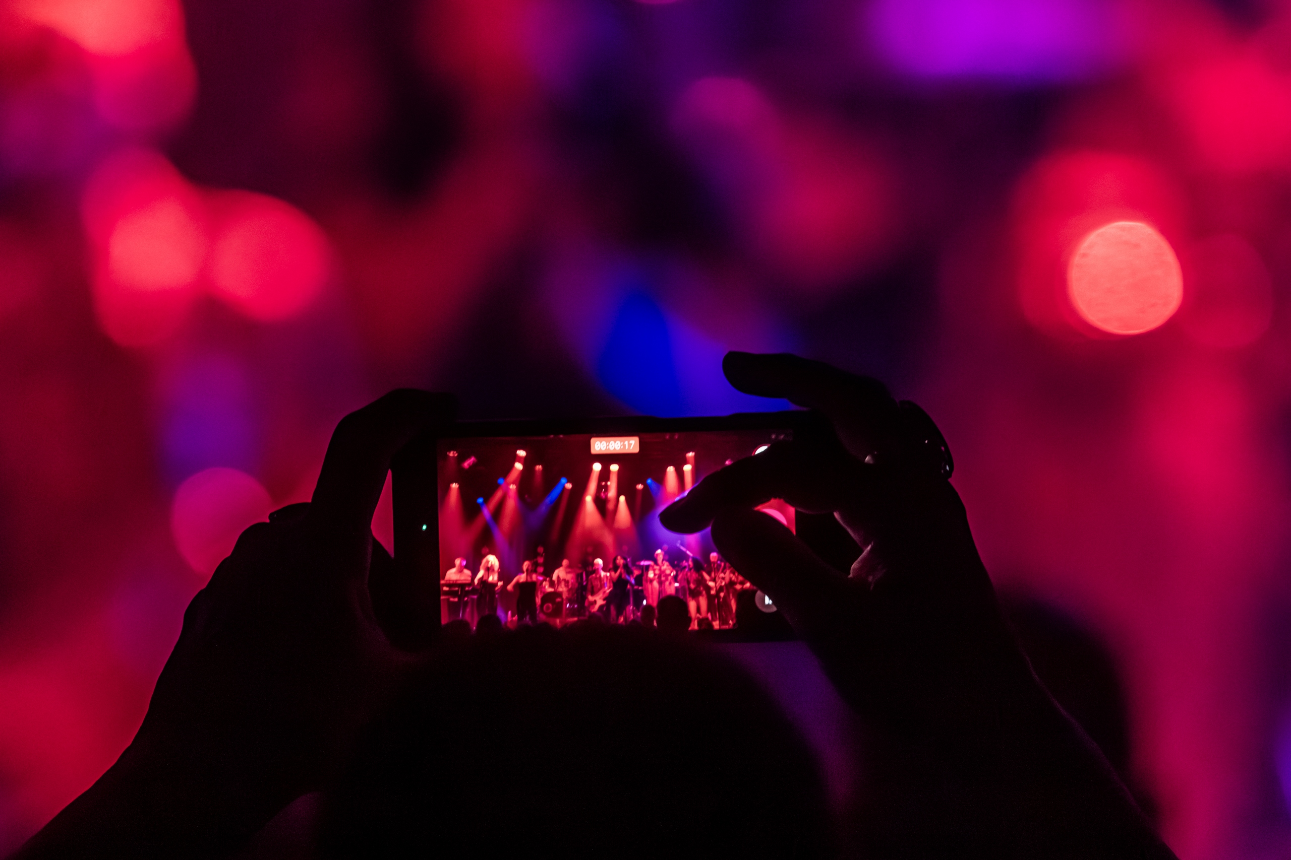 Bezoeker filmt het optreden met een telefoon, met het verlichte podium op de achtergrond