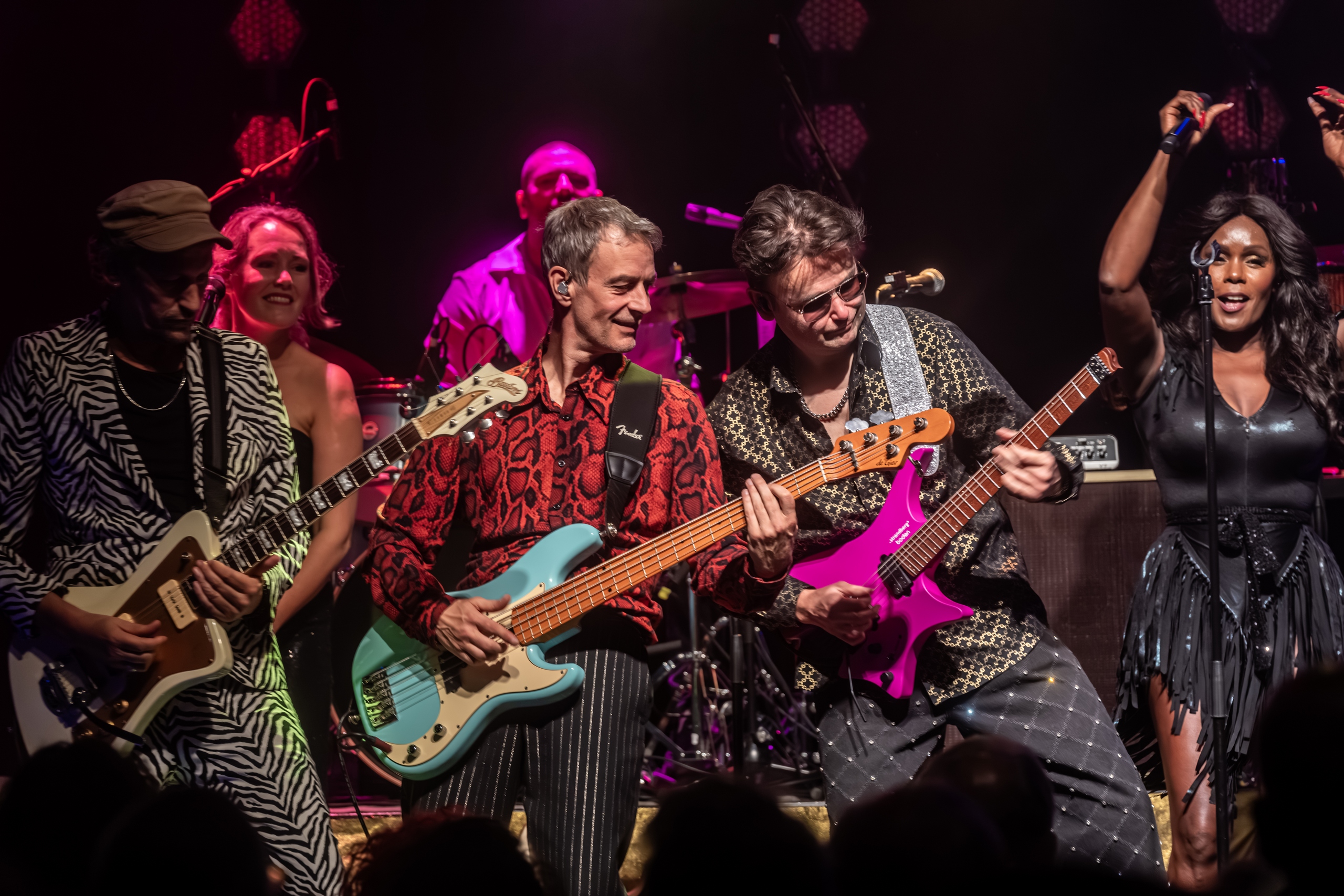 Gitarist en bassist spelen samen vooraan op het podium in roze licht