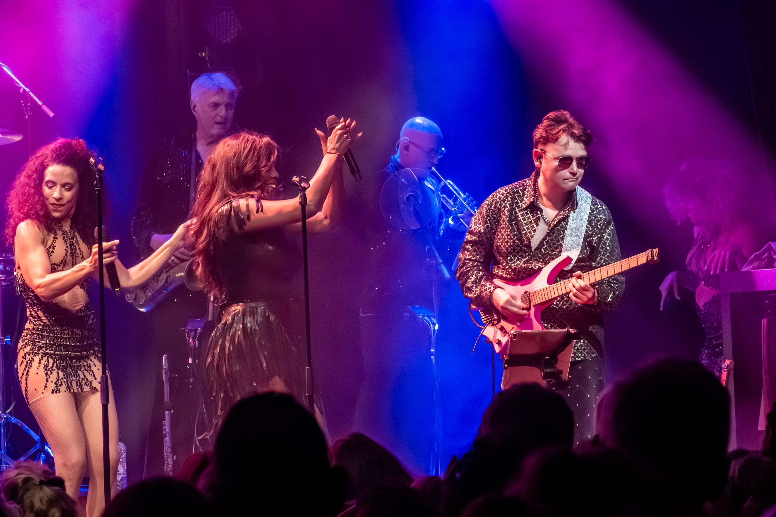 Zangeressen klappen mee terwijl de gitarist soleert in magenta en blauw licht