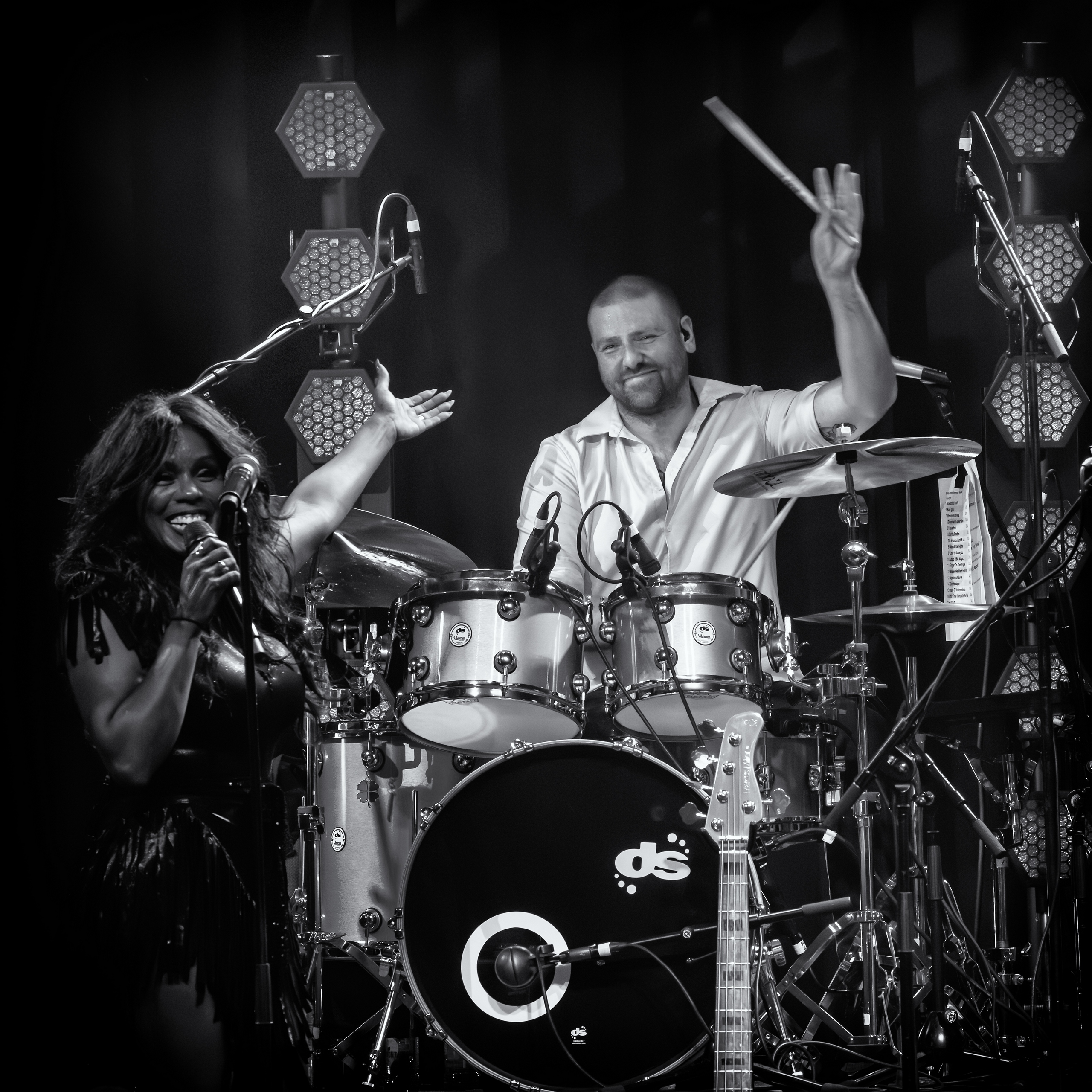 Zwart-witbeeld van de drummer met opgeheven stok naast de zangeres