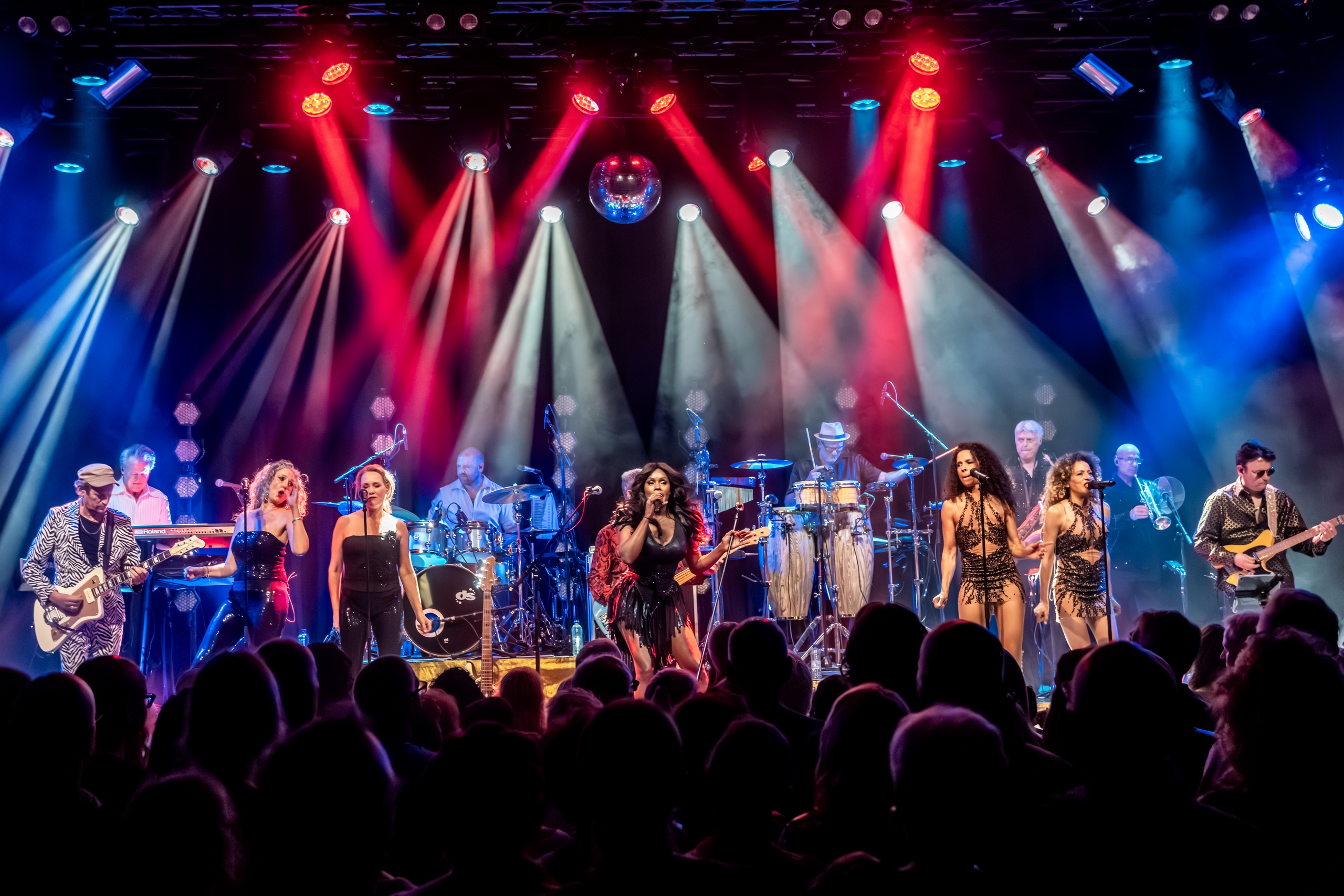 De voltallige band van Donna's Hot Stuff in rode en blauwe lichtbundels boven een volle zaal