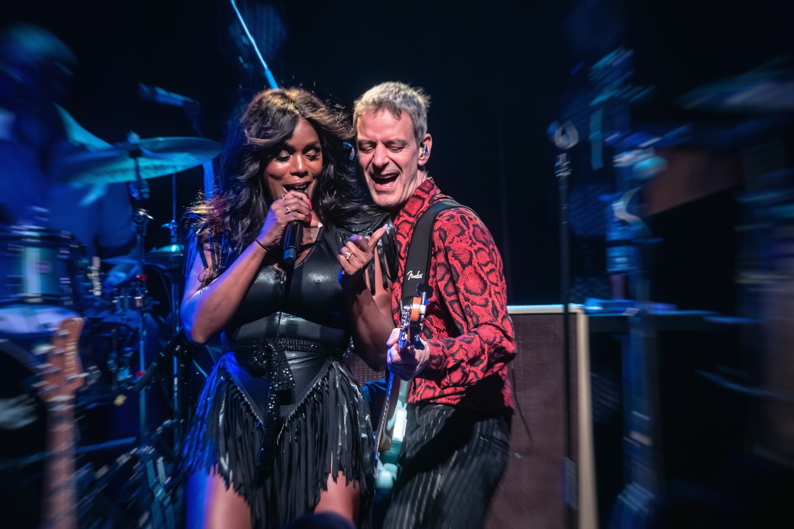 Irma Derby zingt samen met een bandlid in blauw tegenlicht